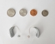 2 real hearing aids laying flat on a table next to coins to show scale