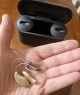 2 beige genesis hearing aids side by side in palm of hand with charger in the background