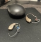 right and left lumity hearing aids laying flat on table next to charger