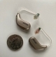 Pair of Oticon Intent 1 hearing aids next to a quarter for scale