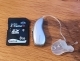 A single right audeo sphere 90 hearing aid laying flat on table next to a sandisk data storage device, showing small size