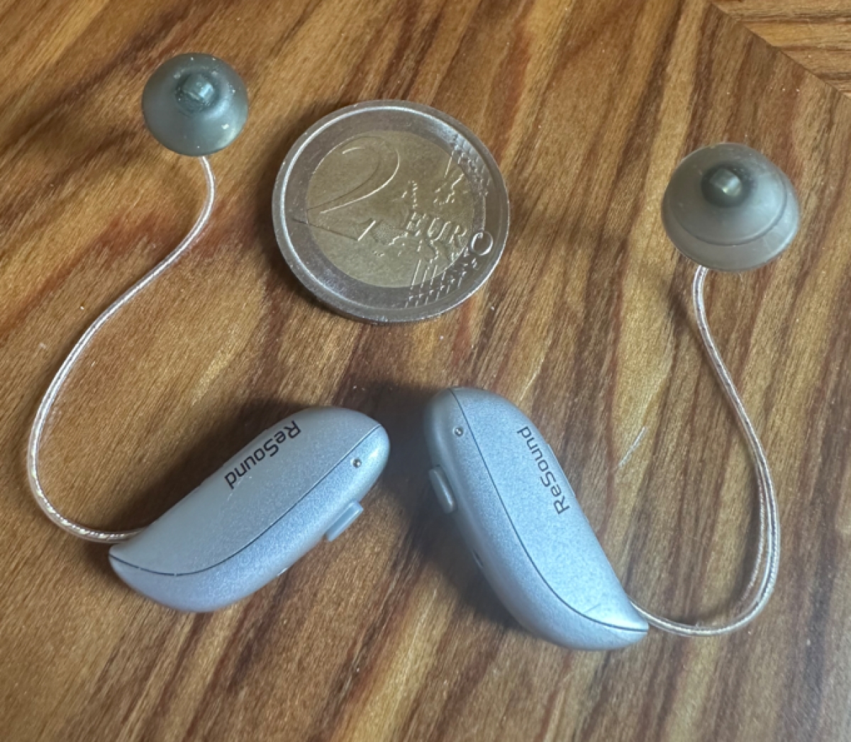 pair of resound vivia 9 in sparkling silver next to coin