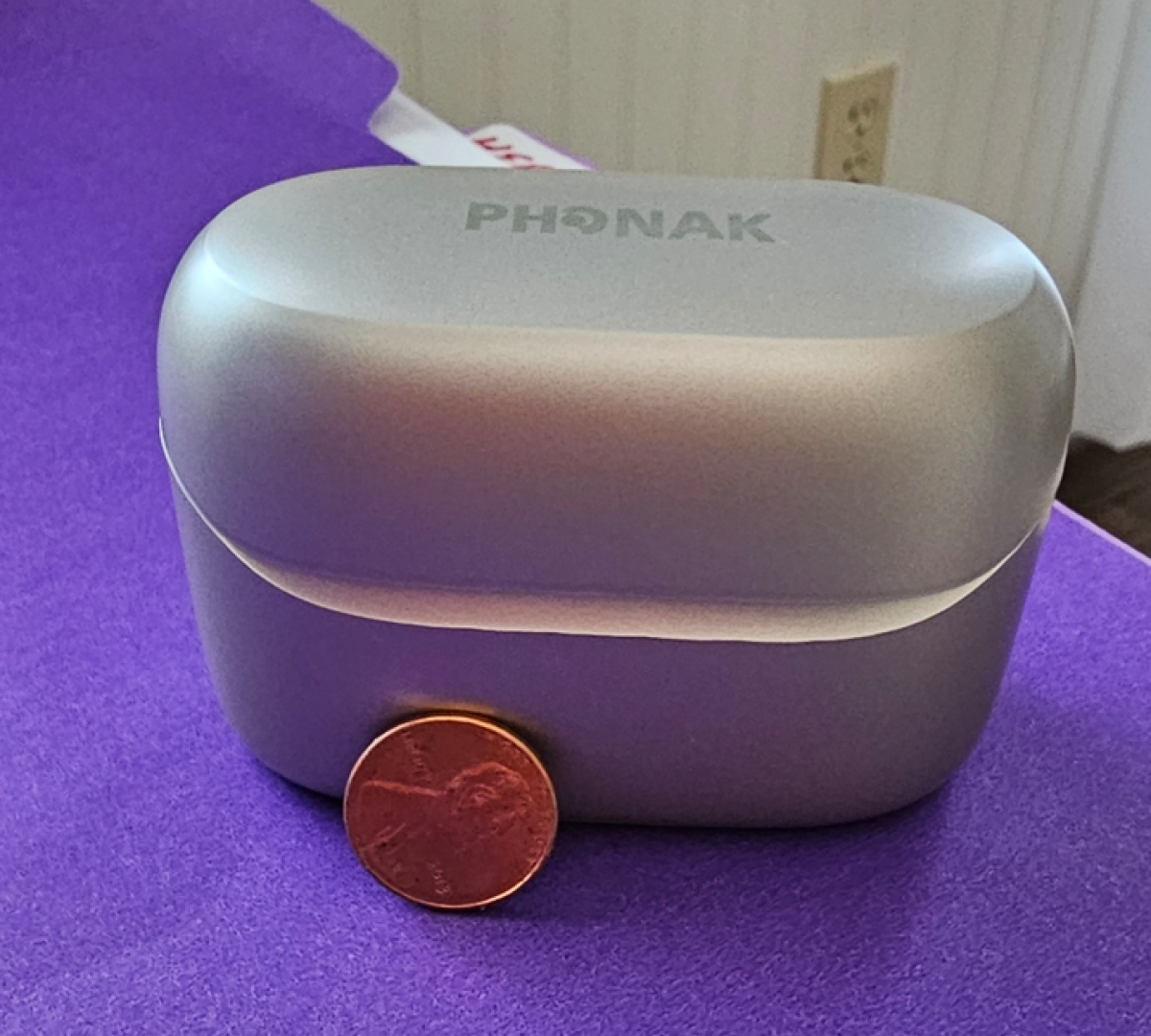 Phonak infinio ultra sphere charger closed next to penny for scale