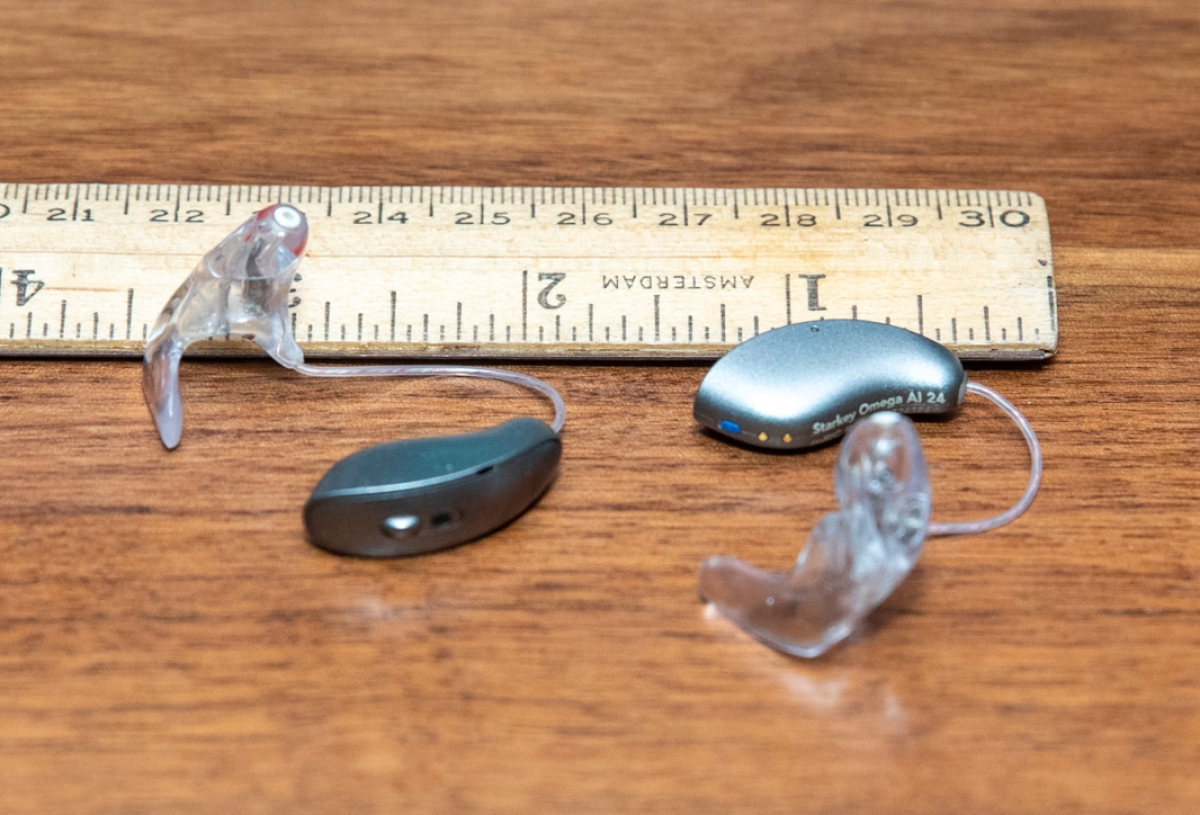 Starkey Omega AI 24 in graphite grey with earmolds attached on table next to ruler