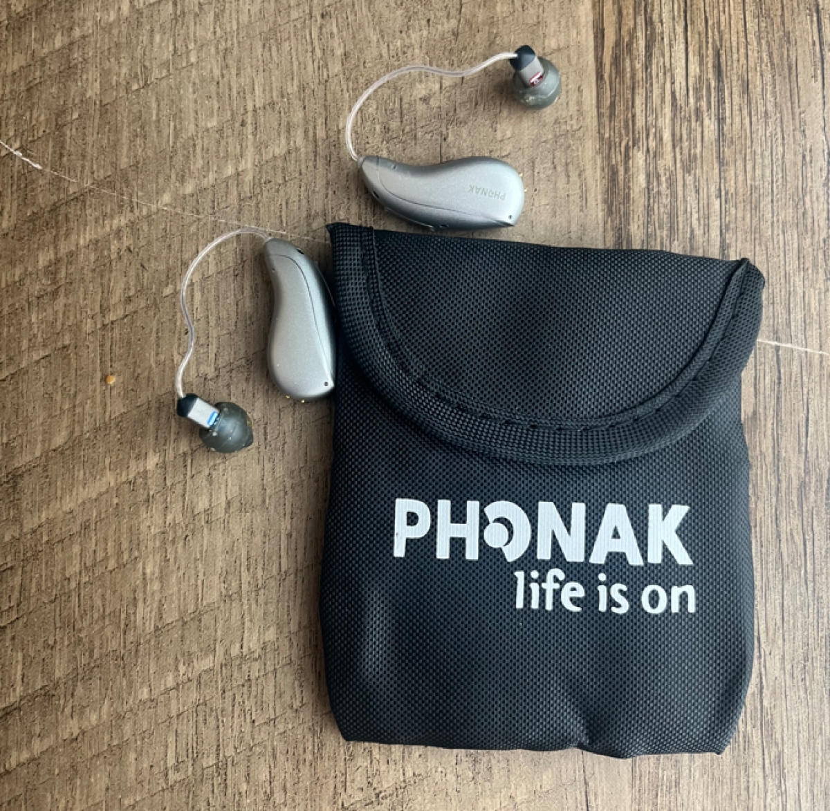 Pair of Phonak Audeo Infinio Ultra Sphere 90 in silver grey next to carry pouch on table