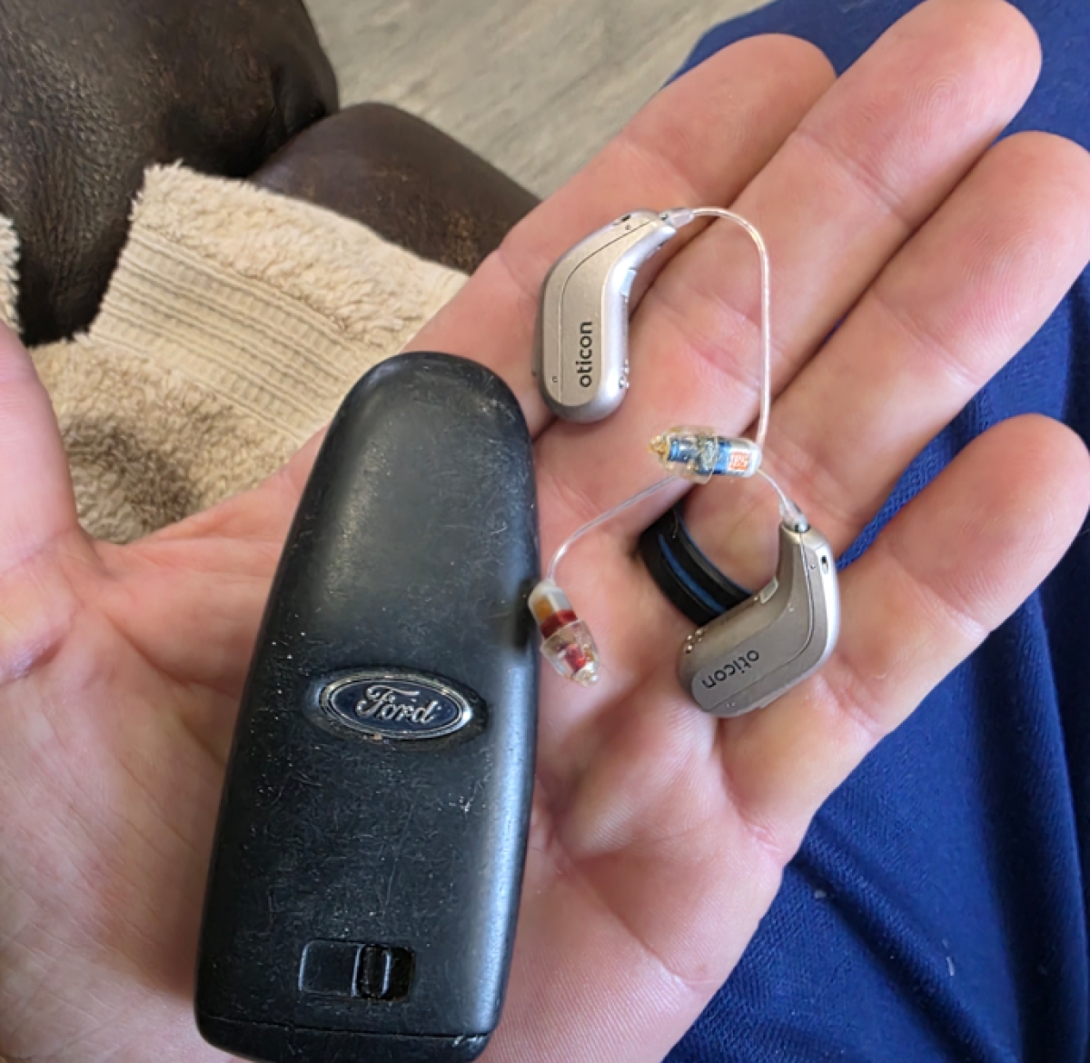 Pair of Oticon Reveal 2 in chroma beige in hand next to car keyfob